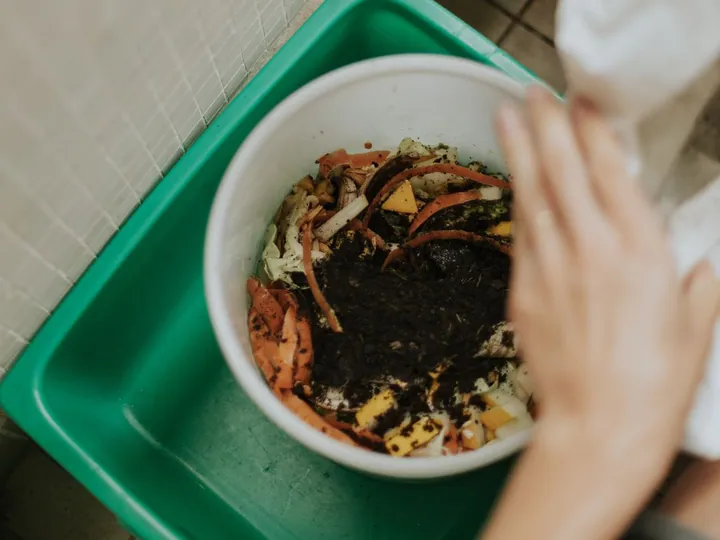 Food scraps being tipped into a small compost container